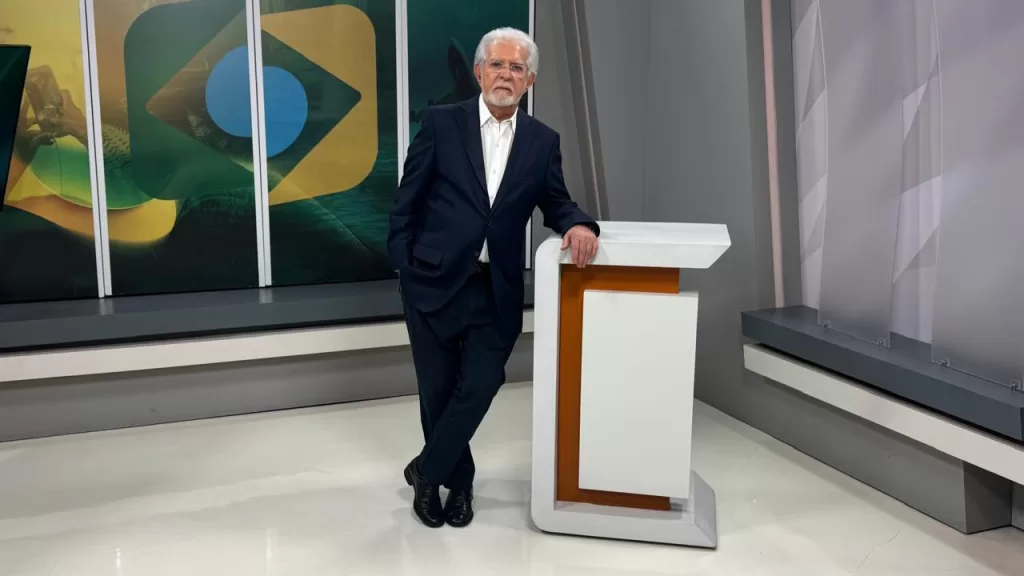 Na imagem, vemos o apresentador Domingos Meireles apoiado em uma bancada do programa Destino Brasil.