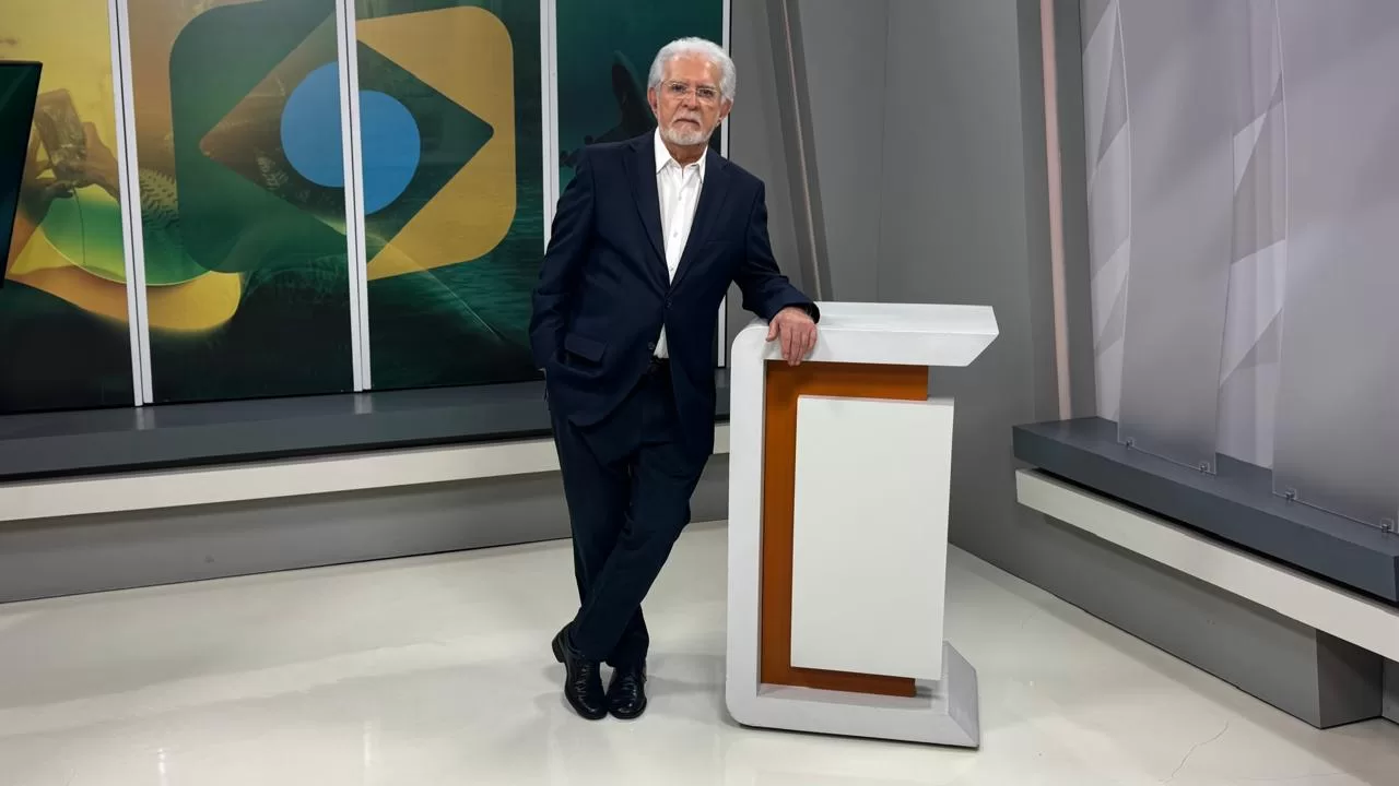 Na imagem, vemos o apresentador Domingos Meireles apoiado em uma bancada do programa Destino Brasil.